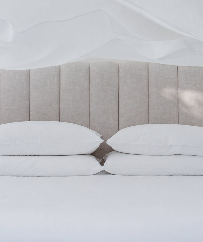 White bedding with stacked pillows beneath a softly tossed sheet.