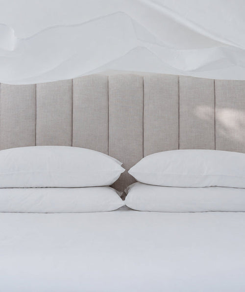 White bedding with stacked pillows beneath a softly tossed sheet.